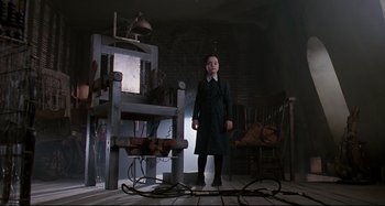 Movie still from “The Addams Family” (1991), directed by Barry Sonnenfeld – A person standing in front of a chair in a room; Medium shot, Low angle