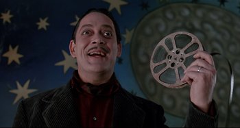 Movie still from “The Addams Family” (1991), directed by Barry Sonnenfeld – A person holding a film reel; Close Up shot, Low angle