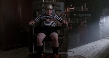 Movie still from “The Addams Family” (1991), directed by Barry Sonnenfeld – A young boy sitting in a chair wearing a helmet; Medium shot, Low angle