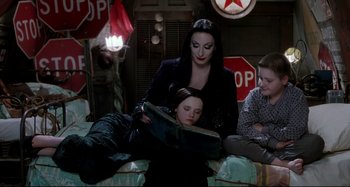 Movie still from “The Addams Family” (1991), directed by Barry Sonnenfeld – A group of people that are sitting on the ground; Medium shot, High angle