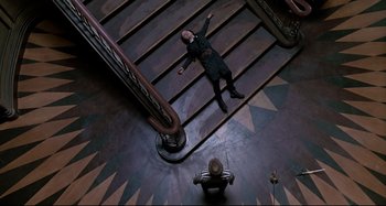 Movie still from “The Addams Family” (1991), directed by Barry Sonnenfeld – A man is laying down on the stairs; Wide shot, Overhead angle