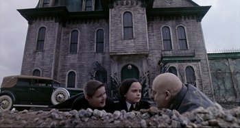 Movie still from “The Addams Family” (1991), directed by Barry Sonnenfeld – A group of people standing next to each other near a building; Wide shot, Low angle