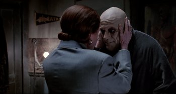 Movie still from “The Addams Family” (1991), directed by Barry Sonnenfeld – A woman putting makeup on a man's face in front of a mirror; Close Up shot, Over the shoulder angle