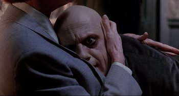Movie still from “The Addams Family” (1991), directed by Barry Sonnenfeld – A man with a bald bald head covering his face with his hands; Close Up shot, Over the shoulder angle