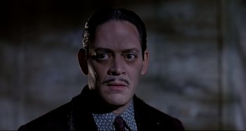 Movie still from “The Addams Family” (1991), directed by Barry Sonnenfeld – A person wearing a suit and tie; Close Up shot, Low angle