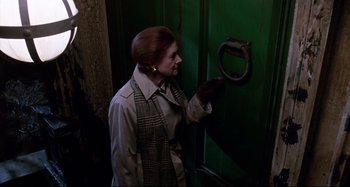 Movie still from “The Addams Family” (1991), directed by Barry Sonnenfeld – A woman in a trench coat looking at a door handle; Medium shot, High angle