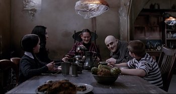 Movie still from “The Addams Family” (1991), directed by Barry Sonnenfeld – A group of people sitting at a table with food; Medium shot, High angle