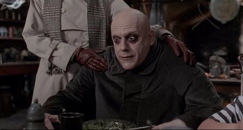 Movie still from “The Addams Family” (1991), directed by Barry Sonnenfeld – A man with a bald head is sitting next to another man; Medium shot, Low angle