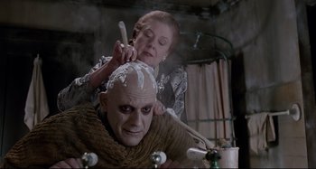 Movie still from “The Addams Family” (1991), directed by Barry Sonnenfeld – A woman cutting a man's hair with a knife; Medium shot, Low angle