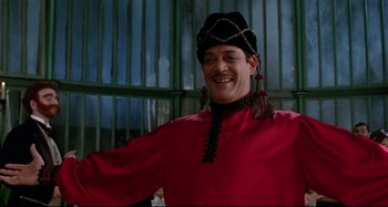 Movie still from “The Addams Family” (1991), directed by Barry Sonnenfeld – A man in a red shirt and a black hat smiling; Medium shot, Low angle