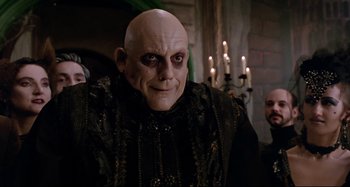 Movie still from “The Addams Family” (1991), directed by Barry Sonnenfeld – A man with a bald head wearing a black outfit; Medium shot, Low angle