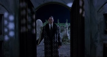 Movie still from “The Addams Family” (1991), directed by Barry Sonnenfeld – A man dressed in a suit and tie holding a giant toothbrush in his hand; Medium shot, Low angle