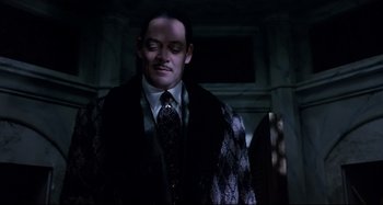 Movie still from “The Addams Family” (1991), directed by Barry Sonnenfeld – A man in a suit and tie standing in front of a window; Medium shot, Low angle