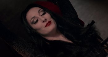 Movie still from “The Addams Family” (1991), directed by Barry Sonnenfeld – A woman with long black hair and red lipstick; Close Up shot, Overhead angle