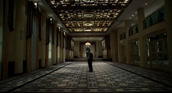 Movie still from “The Adjustment Bureau” (2011), directed by George Nolfi – A man standing in the middle of a large room; Extreme Wide shot, Low angle