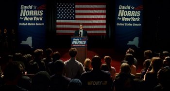 Movie still from “The Adjustment Bureau” (2011), directed by George Nolfi – A man is giving a speech in front of an american flag; Wide shot, High angle