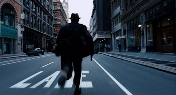 Movie still from “The Adjustment Bureau” (2011), directed by George Nolfi – A man wearing a hat and a black coat walking down a street; Wide shot, Overhead angle