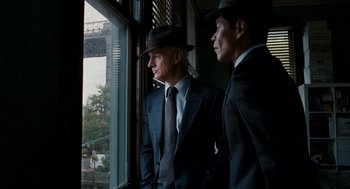 Movie still from “The Adjustment Bureau” (2011), directed by George Nolfi – A couple of men standing next to each other near a window; Medium shot, Over the shoulder angle
