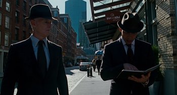 Movie still from “The Adjustment Bureau” (2011), directed by George Nolfi – A man in a suit and a hat standing next to another man in a suit and a hat; Medium shot, Over the shoulder angle