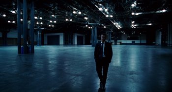 Movie still from “The Adjustment Bureau” (2011), directed by George Nolfi – A man wearing a suit and tie in a large warehouse; Wide shot, High angle