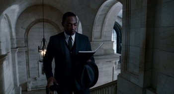 Movie still from “The Adjustment Bureau” (2011), directed by George Nolfi – A man in a suit and hat reading a book; Medium shot, Over the shoulder angle