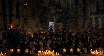 Movie still from “The Adventures of Baron Munchausen” (1988), directed by Terry Gilliam – A group of people sitting in a room with candles; Extreme Wide shot, High angle