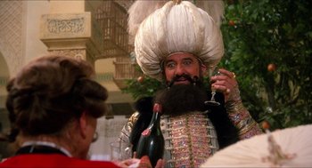 Movie still from “The Adventures of Baron Munchausen” (1988), directed by Terry Gilliam – A man with a beard and a mustache holding a wine glass and a bottle; Medium shot, Over the shoulder angle