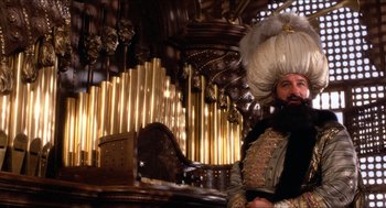 Movie still from “The Adventures of Baron Munchausen” (1988), directed by Terry Gilliam – A man with a beard is sitting at a table; Wide shot, Low angle