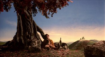 Movie still from “The Adventures of Baron Munchausen” (1988), directed by Terry Gilliam – A man sitting on the ground next to a tree; Wide shot, Low angle