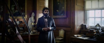 Movie still from “The Aeronauts” (2019), directed by Tom Harper – A man in a suit and tie standing in front of a painting; Medium shot, Low angle