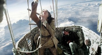 Movie still from “The Aeronauts” (2019), directed by Tom Harper – A woman in a brown jacket is hanging on a rope; Wide shot, Low angle