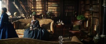 Movie still from “The Aeronauts” (2019), directed by Tom Harper – A woman sitting on a couch in front of a book case; Wide shot, High angle