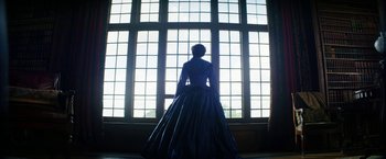 Movie still from “The Aeronauts” (2019), directed by Tom Harper – A woman in a blue dress standing in front of a window; Wide shot, Low angle