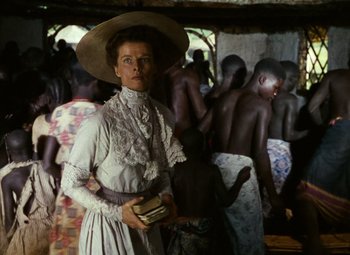 Movie still from “The African Queen” (1951), directed by John Huston – A woman wearing a hat standing in front of a group of people; Medium shot, Low angle