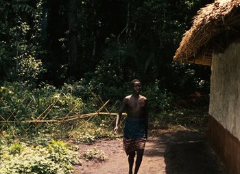 Movie still from “The African Queen” (1951), directed by John Huston – A man walking down a dirt path near a hut; Extreme Wide shot, Over the shoulder angle