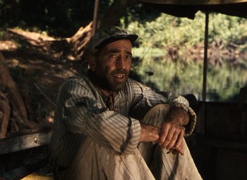 Movie still from “The African Queen” (1951), directed by John Huston – A man sitting on the ground with his hands on his knees; Close Up shot, High angle