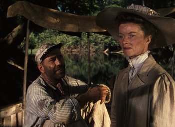 Movie still from “The African Queen” (1951), directed by John Huston – A man and a woman standing next to each other under an awning; Medium shot, Low angle