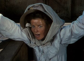 Movie still from “The African Queen” (1951), directed by John Huston – A woman in a white jacket is holding her arms up; Medium shot, Low angle