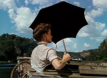 Movie still from “The African Queen” (1951), directed by John Huston – A woman holding an umbrella while sitting on a boat; Medium shot, Low angle