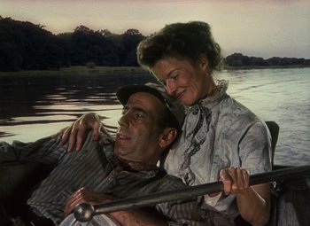 Movie still from “The African Queen” (1951), directed by John Huston – An older man and a younger woman are rowing a boat on a lake; Medium shot, High angle