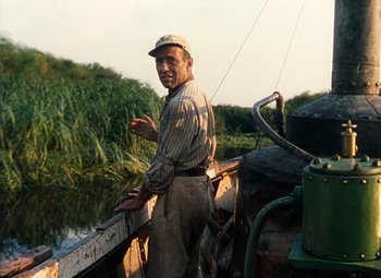 Movie still from “The African Queen” (1951), directed by John Huston – An older man standing on a boat in the water; Medium shot, High angle