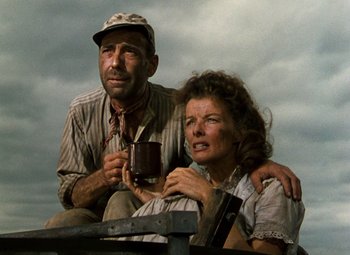 Movie still from “The African Queen” (1951), directed by John Huston – An older man and woman sitting next to each other holding cups; Medium shot, Low angle