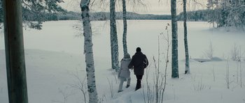 Movie still from “The American” (2010), directed by Anton Corbijn – Two people are walking in the snow near some trees; Wide shot, High angle