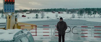 Movie still from “The American” (2010), directed by Anton Corbijn – A man standing in front of an open gate in the snow; Wide shot, High angle