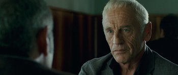 Movie still from “The American” (2010), directed by Anton Corbijn – An older man with white hair and blue eyes looking at the camera; Close Up shot, Over the shoulder angle