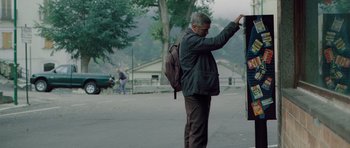 Movie still from “The American” (2010), directed by Anton Corbijn – A man standing on the side of the road with a backpack; Wide shot, Over the shoulder angle