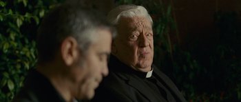 Movie still from “The American” (2010), directed by Anton Corbijn – Two men sitting next to each other in front of a tree; Close Up shot, Over the shoulder angle
