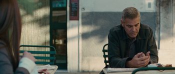 Movie still from “The American” (2010), directed by Anton Corbijn – An older man sitting at an outside table; Medium shot, Over the shoulder angle
