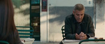 Movie still from “The American” (2010), directed by Anton Corbijn – An older man sitting at an outdoor table; Medium shot, Over the shoulder angle