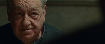 Movie still from “The American” (2010), directed by Anton Corbijn – An old man with a gray beard and a gray shirt; Close Up shot, Over the shoulder angle